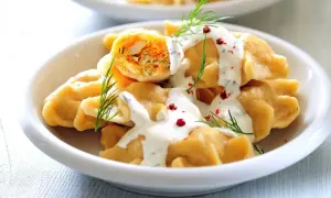 Pyszne pierogi z warzywnym farszem, polane sosem jogurtowym z koperkiem i posypane pieprzem. Idealny pomysł na obiad bez mięsa.