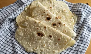 Placki tortilla oryginalny przepis. Świeżo upieczone, lekko przypieczone placki tortilli ułożone na kratkowanym ręczniku.