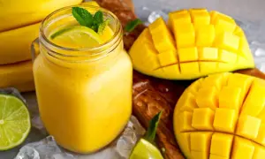 Orzeźwiający koktajl z mango, udekorowany miętą i limonką, obok pokrojonych owoców i bananów.