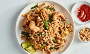 Pyszny sos pad thai z krewetkami, orzeszkami ziemnymi i limonką. Obok miseczka z chili i orzeszkami.