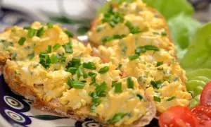 Pyszna pasta jajeczna jak dawniej, na chlebie, posypana szczypiorkiem. Obok sałata i pomidorki.