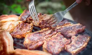 Soczysty boczek na grillu, idealny po marynacie. Dwie widelce pomagają w obracaniu kawałków.