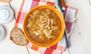 Stary przepis na flaki po zamojsku. Aromatyczna zupa z kawałkami flaków i marchewki, podana z chlebem na kratkowanej serwetce.