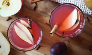 Dwa kieliszki aromatycznego kompotu z jabłek, gruszek i śliwek, ozdobione laskami cynamonu i goździkami.
