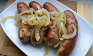 Pieczona biała kiełbasa surowa z cebulą na białym talerzu.