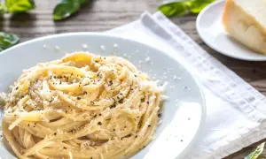 Pyszne danie z makaronem, posypane startym parmezanem i świeżo mielonym pieprzem, z listkami bazylii i kawałkiem sera w tle.