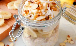 Słoik pełen pysznej owsianki z bananem, posypanej wiórkami kokosowymi i orzechami. Idealne śniadanie!