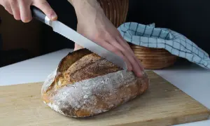 Ręce kroją świeżo upieczony bochenek chleba na zakwasie. Stary przepis na chleb na zakwasie ożywa na desce.