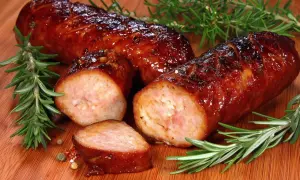 Pyszna, rumiana kiełbasa z piekarnika, pokrojona w plastry, z gałązkami rozmarynu i ziarnami pieprzu na desce.