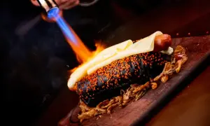 Gorący piesek w czarnej bułce z sezamem, topiony ser i chrupiąca cebulka. Płomienie z palnika podkreślają efekt flambirowania.