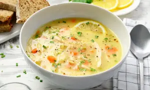 Aromatyczna zupa cytrynowa z kurczakiem, marchewką i fasolką, ozdobiona plasterkiem cytryny i natką pietruszki. Podana z chlebem.