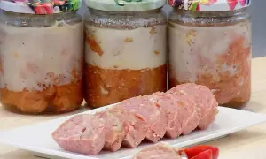 Trzy słoiki domowej kiełbasy w galarecie, obok pokrojona kiełbasa na talerzyku.