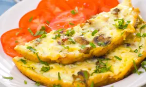 Puszysty omlet z pieczarkami i natką pietruszki, podany z plastrami pomidora. Idealne śniadanie.