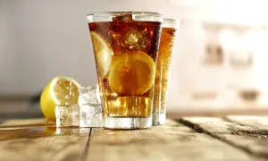 Dwa orzeźwiające drinki Long Island Ice Tea z plasterkami cytryny i kostkami lodu na drewnianym blacie.