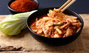 Misternie przygotowane kimchi, czyli co to jest? Miska pełna pikantnej, fermentowanej kapusty pekińskiej, obok świeża główka i miseczka czerwonych przypraw.