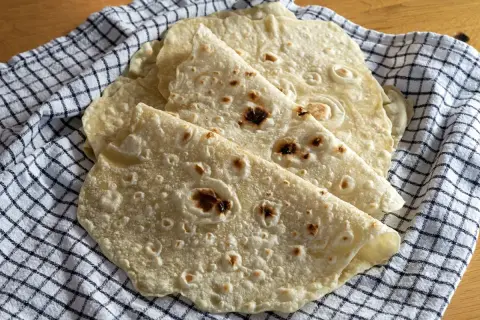 Placki tortilla oryginalny przepis. Świeżo upieczone, lekko przypieczone placki tortilli ułożone na kratkowanym ręczniku.