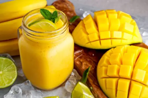 Orzeźwiający koktajl z mango, udekorowany miętą i limonką, obok pokrojonych owoców i bananów.