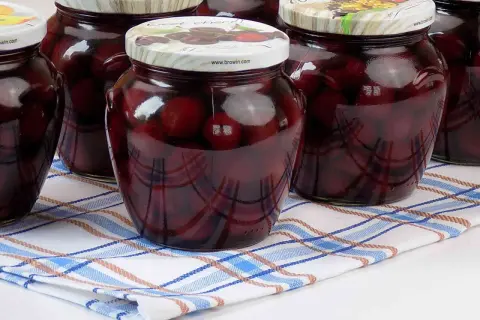 Słoiki z domowym kompotem z czereśni, gotowe na zimę. Ciemne owoce w słodkim syropie.