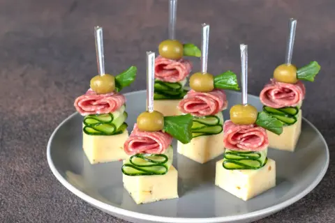 Koreczki na przyjęcie: ser, salami, ogórek, oliwka i listek ziół na wykałaczce.