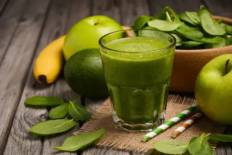Zielony koktajl owocowy z jabłkiem, bananem i awokado, obok świeżego szpinaku.
