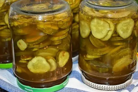 Słoiki pełne plasterków ogórków w zalewie z curry, ze skórką, gotowe do spożycia.