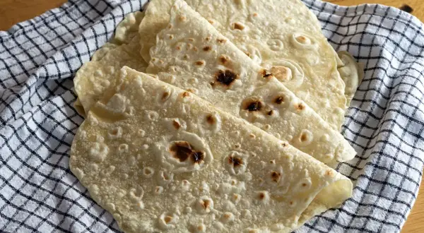 Placki tortilla oryginalny przepis. Świeżo upieczone, lekko przypieczone placki tortilli ułożone na kratkowanym ręczniku.