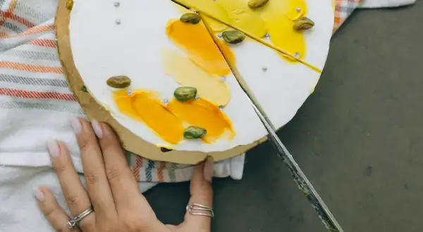 Delikatny tort z pistacjami i żółtym kremem, pokazujący, jak kroić tort.