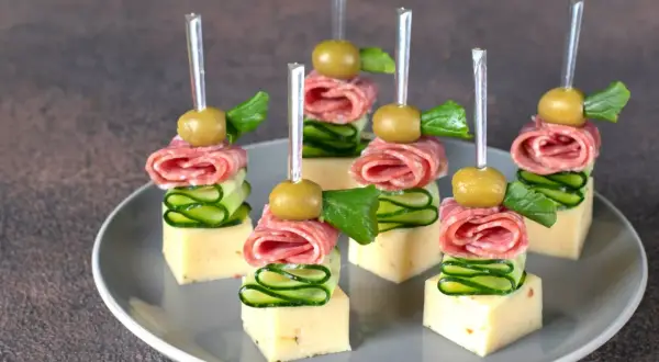 Koreczki na przyjęcie: ser, salami, ogórek, oliwka i listek ziół na wykałaczce.