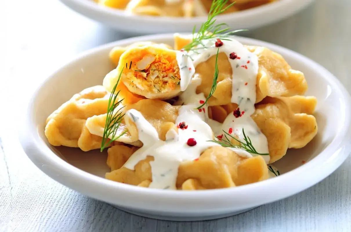 Pyszne pierogi z warzywnym farszem, polane sosem jogurtowym z koperkiem i posypane pieprzem. Idealny pomysł na obiad bez mięsa.