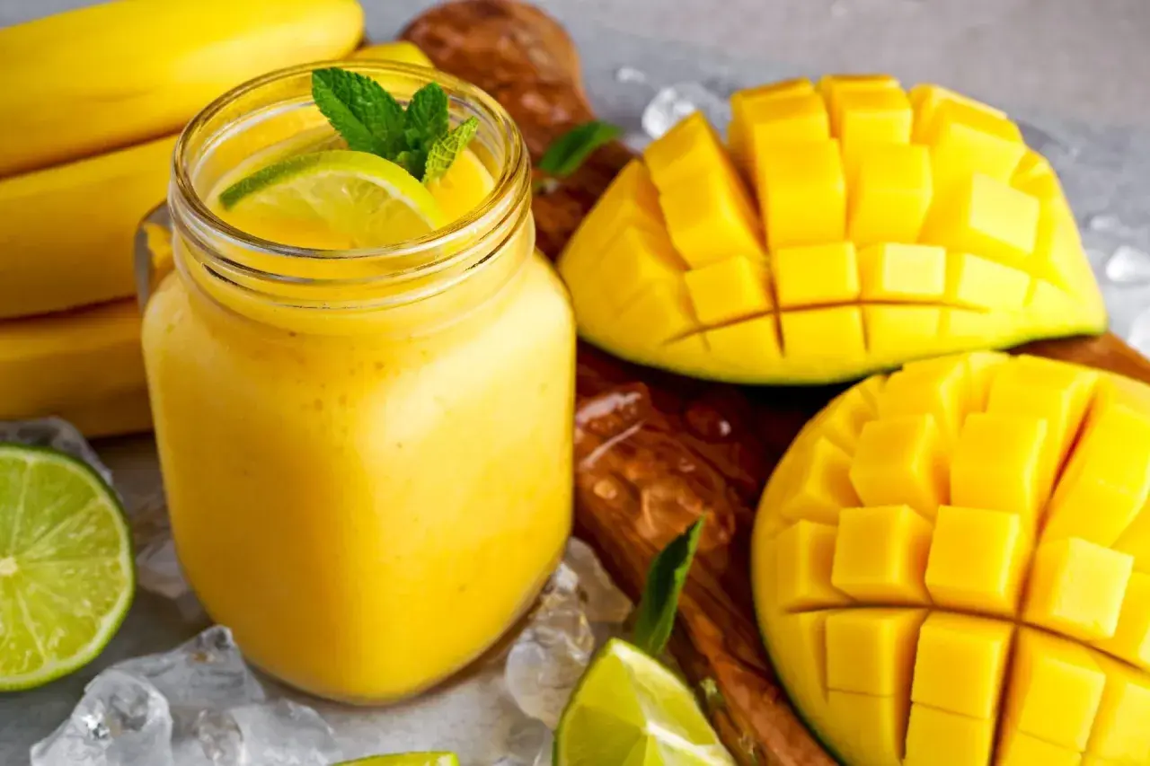 Orzeźwiający koktajl z mango, udekorowany miętą i limonką, obok pokrojonych owoców i bananów.