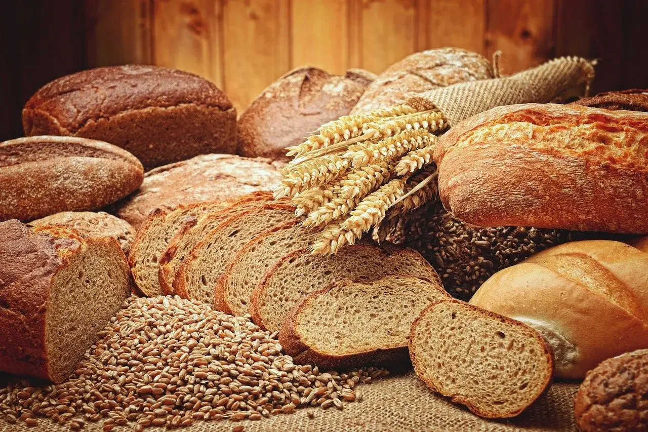 Różnorodne rodzaje chleba, od ciemnych bochenków po pokrojone kromki, leżą obok kłosów zboża.