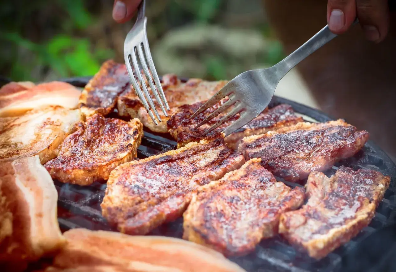 Soczysty boczek na grillu, idealny po marynacie. Dwie widelce pomagają w obracaniu kawałków.