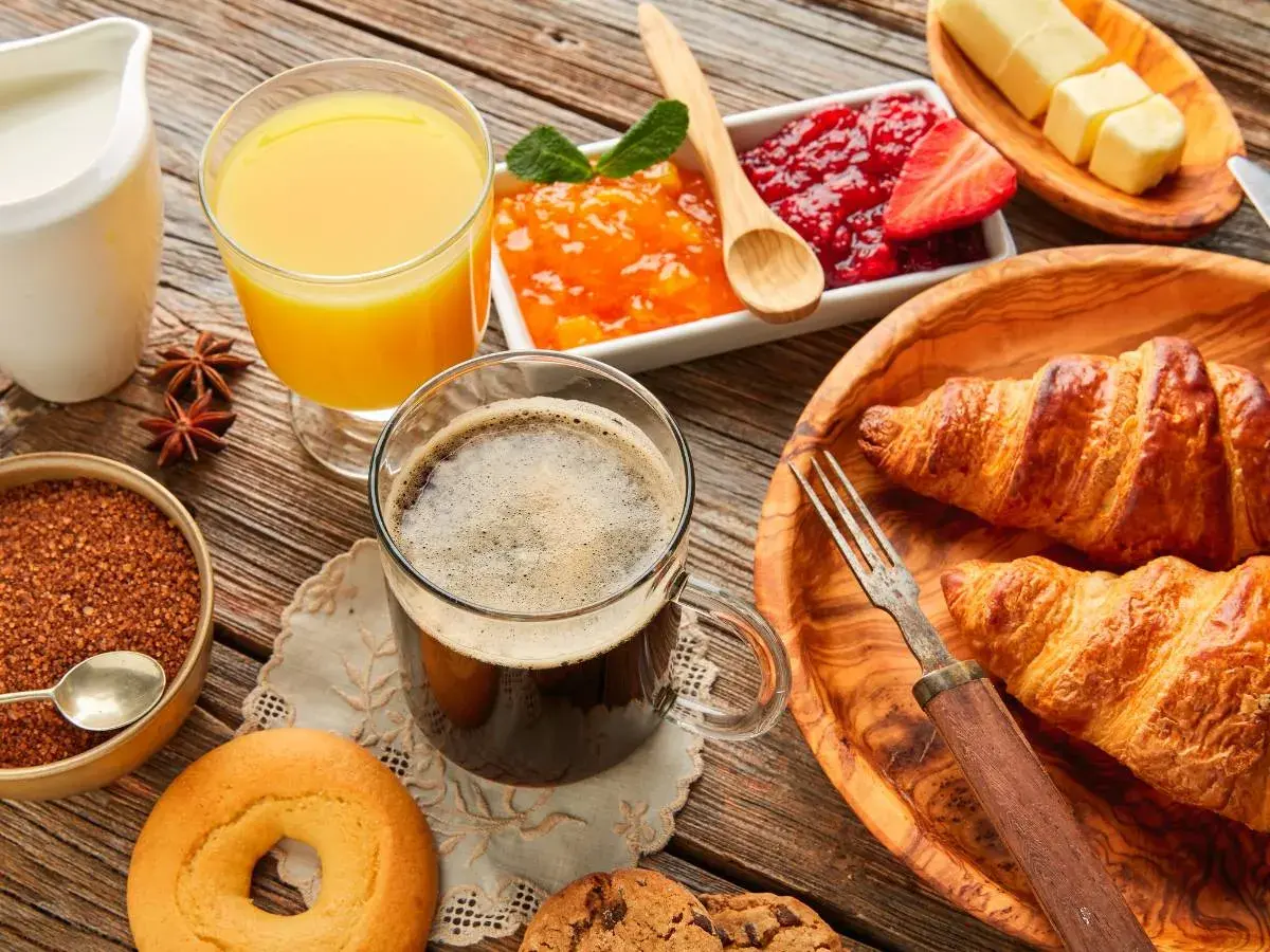 Pyszne śniadanie kontynentalne: świeże croissanty, dżemy, masło, kawa i sok pomarańczowy na drewnianym stole.