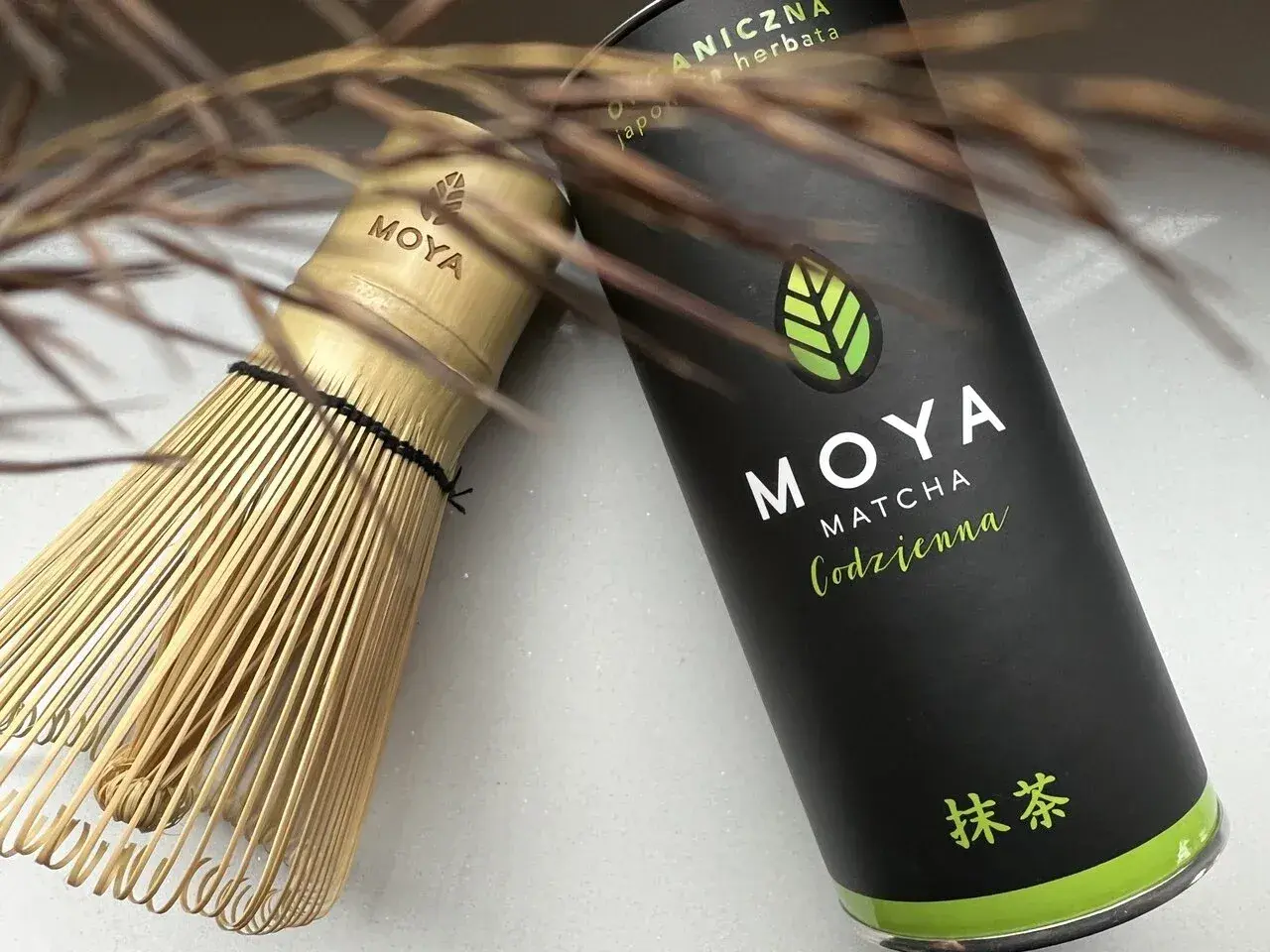 Tradycyjny bambusowy chasen obok puszki MOYA Matcha Codzienna. Idealne narzędzia, by poznać, co to matcha.
