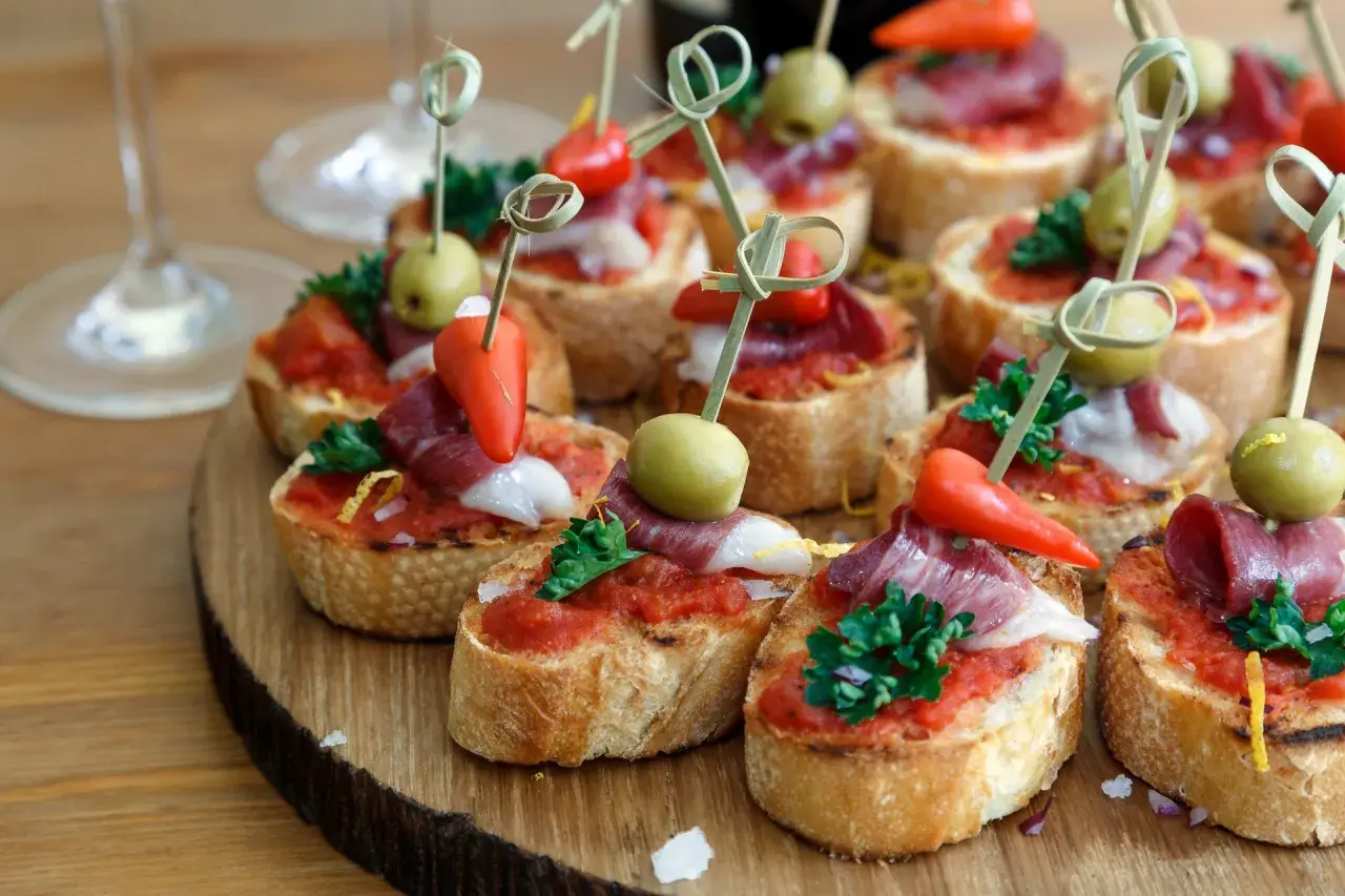 Pyszne finger food: grzanki z pomidorami, szynką, oliwkami i papryczkami, ozdobione natką pietruszki. Idealne na przyjęcie!