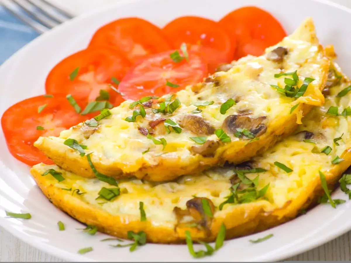 Puszysty omlet z pieczarkami i natką pietruszki, podany z plastrami pomidora. Idealne śniadanie.