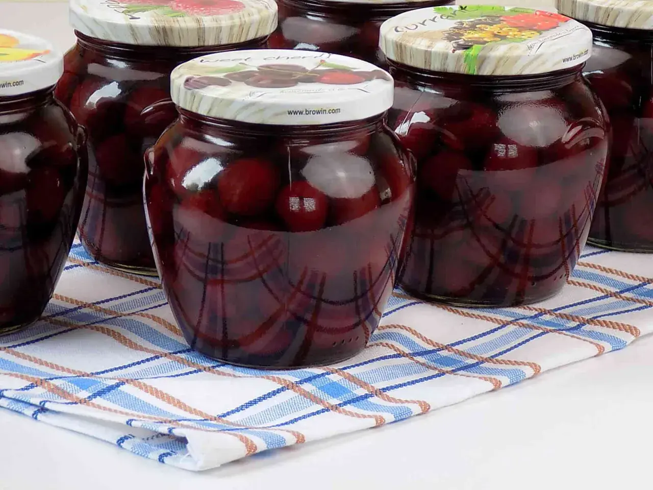 Słoiki z domowym kompotem z czereśni, gotowe na zimę. Ciemne owoce w słodkim syropie.