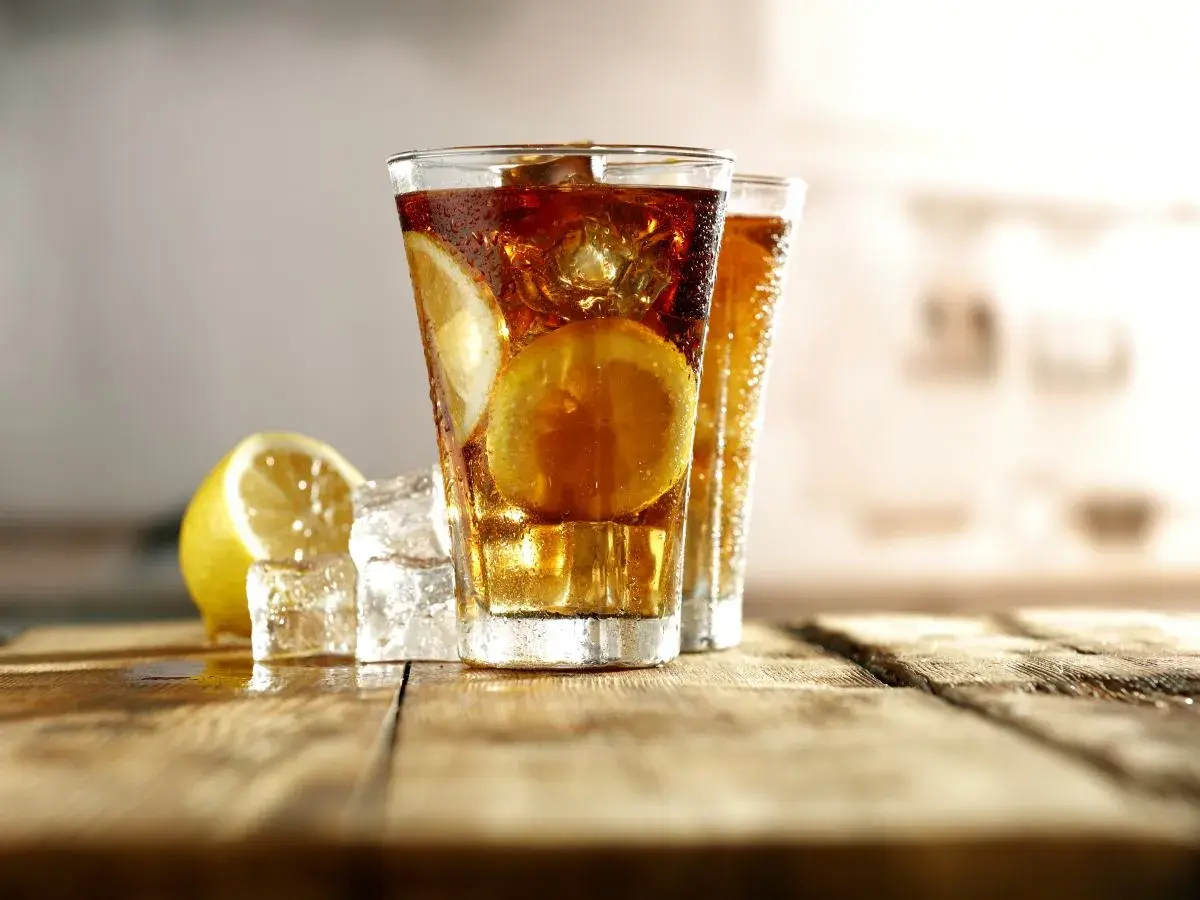 Dwa orzeźwiające drinki Long Island Ice Tea z plasterkami cytryny i kostkami lodu na drewnianym blacie.