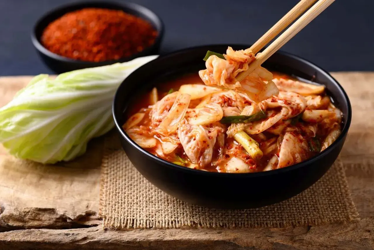 Misternie przygotowane kimchi, czyli co to jest? Miska pełna pikantnej, fermentowanej kapusty pekińskiej, obok świeża główka i miseczka czerwonych przypraw.