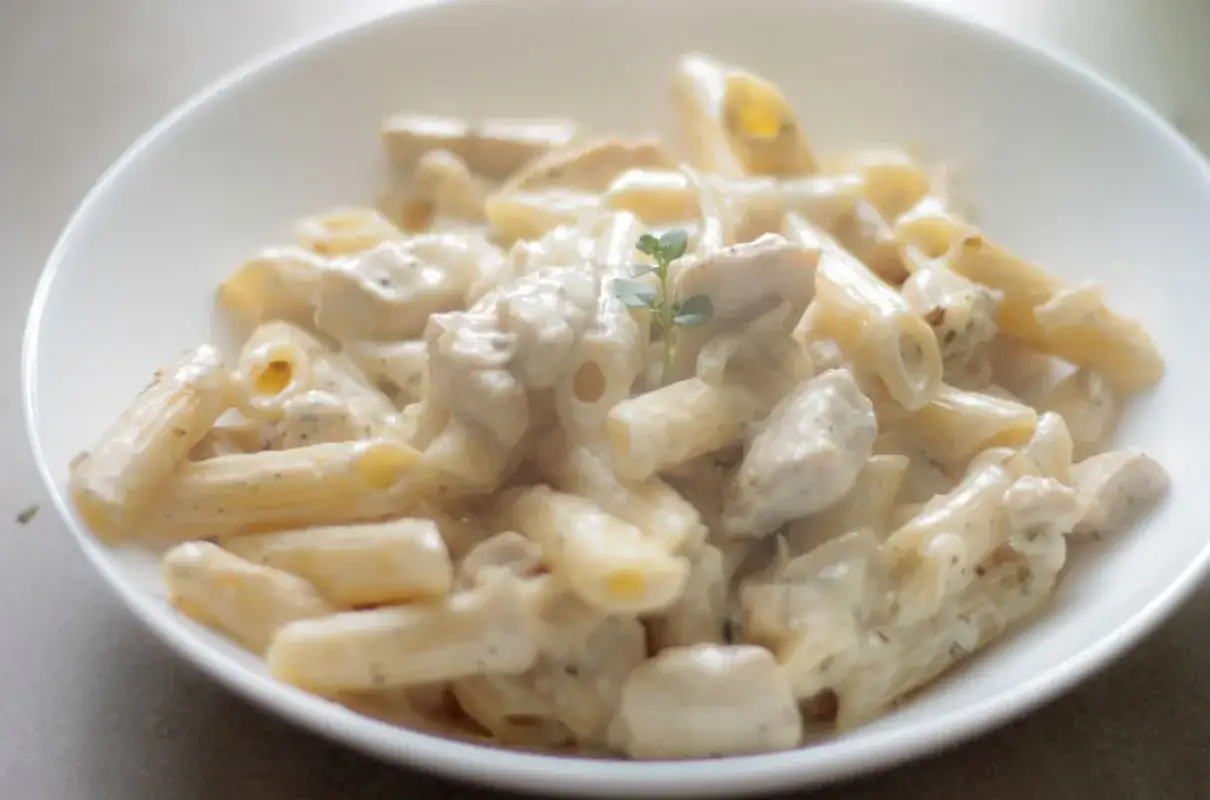 Penne z kurczakiem w kremowym sosie śmietanowo serowym, udekorowane gałązką ziół. Pyszne danie gotowe do podania.