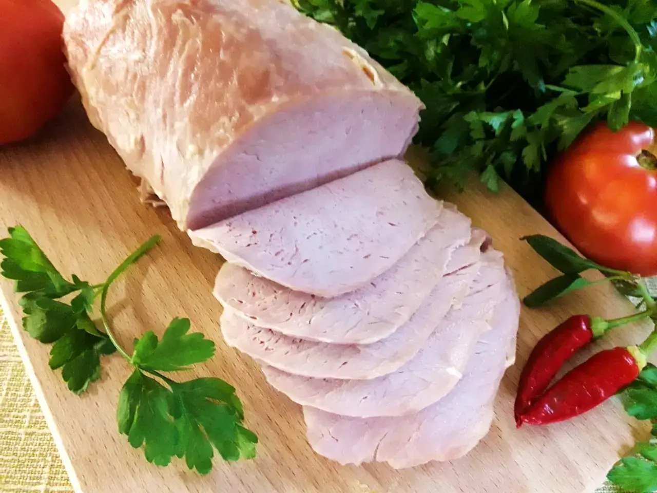 Pokrojony schab gotowany 2 razy po 10 minut, z pomidorami, papryczkami chili i natką pietruszki na desce.