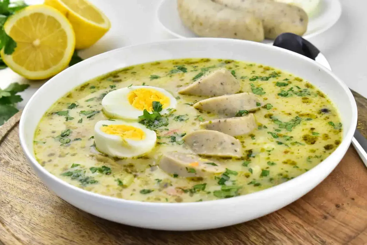 Aromaticzny barszcz chrzanowy z jajkiem i kiełbasą, ozdobiony natką pietruszki. Obok połówki cytryny.