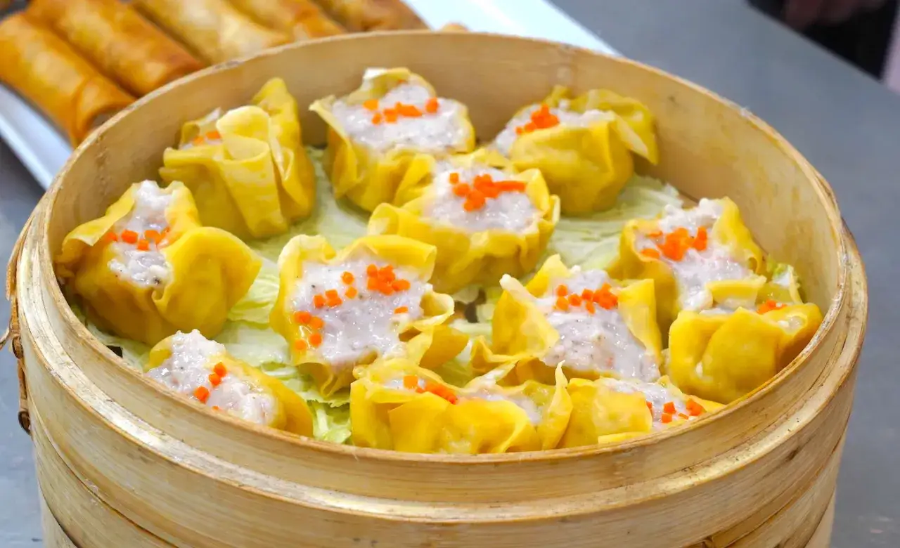 Pyszne dim sum w bambusowym parowniku, ozdobione pomarańczową papryką.