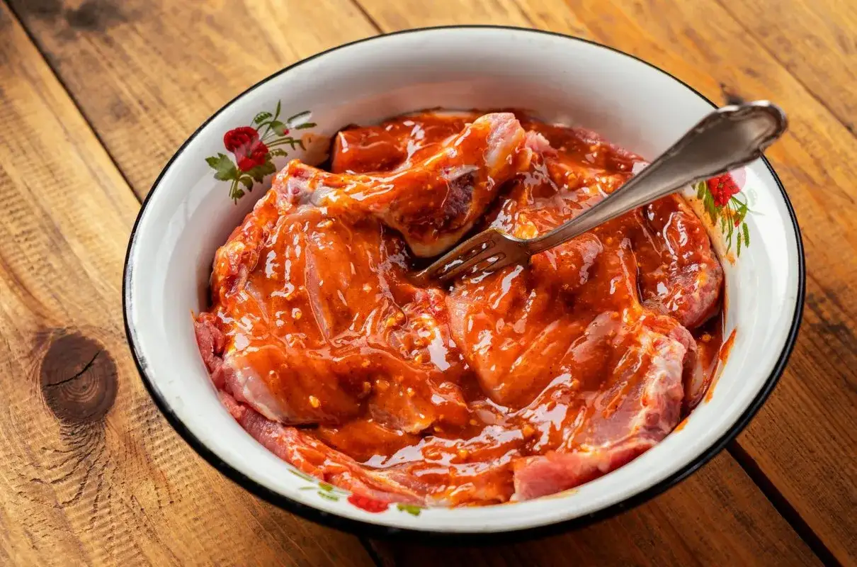 Mięso w misce, gotowe do grillowania. Aromatyczna marynata na grilla otula kawałki mięsa, zapowiadając smakowity posiłek. Widelec czeka, by zamieszać.
