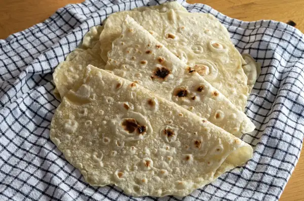 Placki tortilla oryginalny przepis. Świeżo upieczone, lekko przypieczone placki tortilli ułożone na kratkowanym ręczniku.