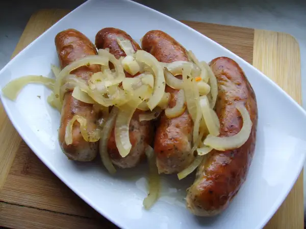 Pieczona biała kiełbasa surowa z cebulą na białym talerzu.