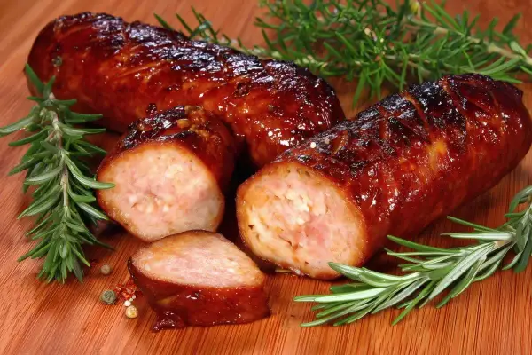 Pyszna, rumiana kiełbasa z piekarnika, pokrojona w plastry, z gałązkami rozmarynu i ziarnami pieprzu na desce.