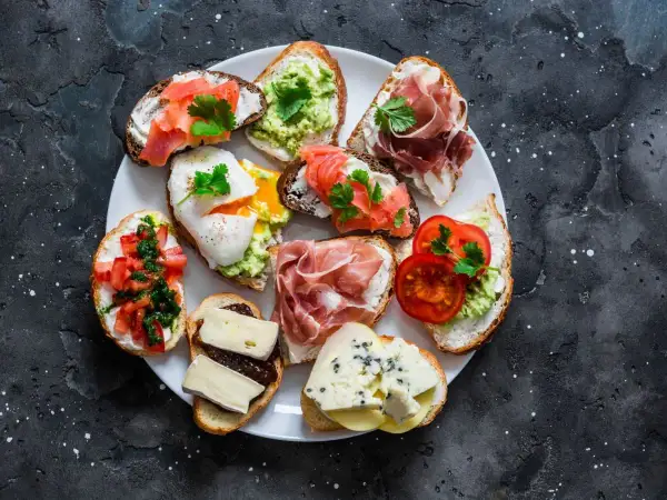 Talerz pełen pysznych sznytek: z łososiem, awokado, jajkiem w koszulce, szynką parmeńską, pomidorami i serami.