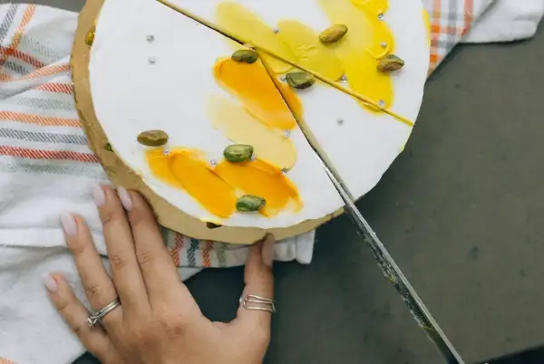 Delikatny tort z pistacjami i żółtym kremem, pokazujący, jak kroić tort.