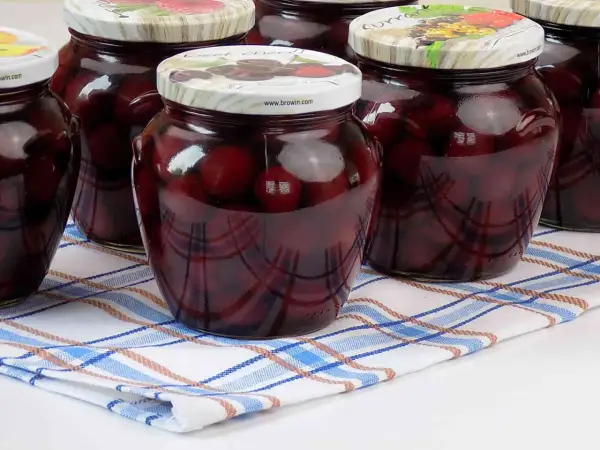 Słoiki z domowym kompotem z czereśni, gotowe na zimę. Ciemne owoce w słodkim syropie.